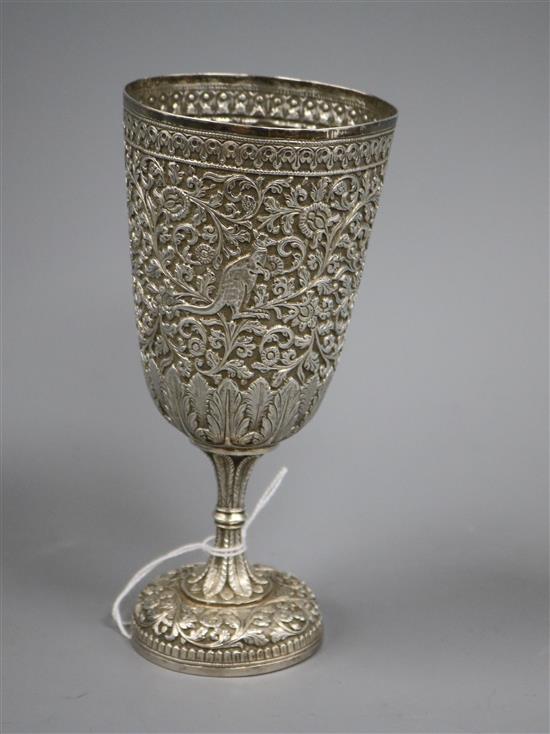 An Indian white metal pedestal cup embossed with animals amid scrolling foliage, stamped VK on the base, 18cm.